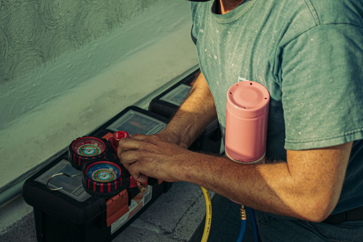 Technician kneeling beside an outdoor HVAC unit during an equipment installation.